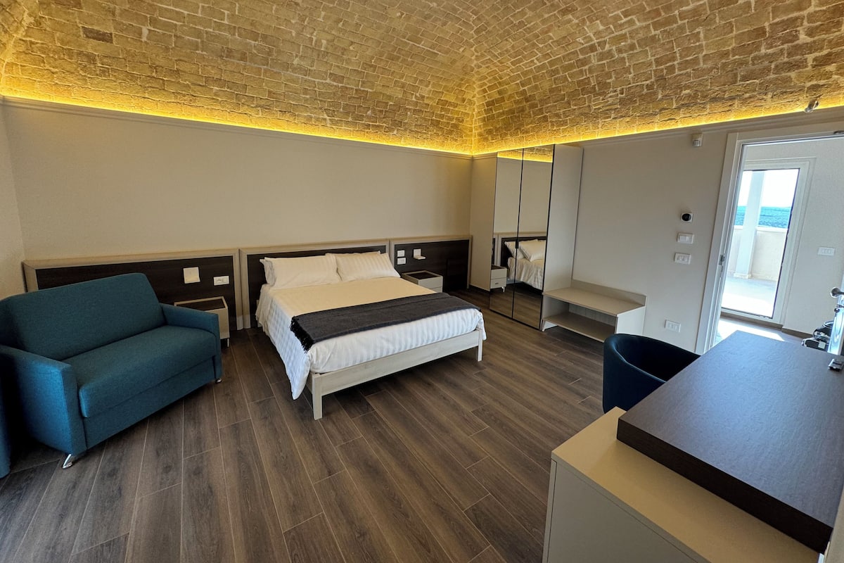 Ein modernes Hotelzimmer mit Backsteinverkleidung, einem großen Bett, einer Couch, einem Schreibtisch und einem Spiegel.