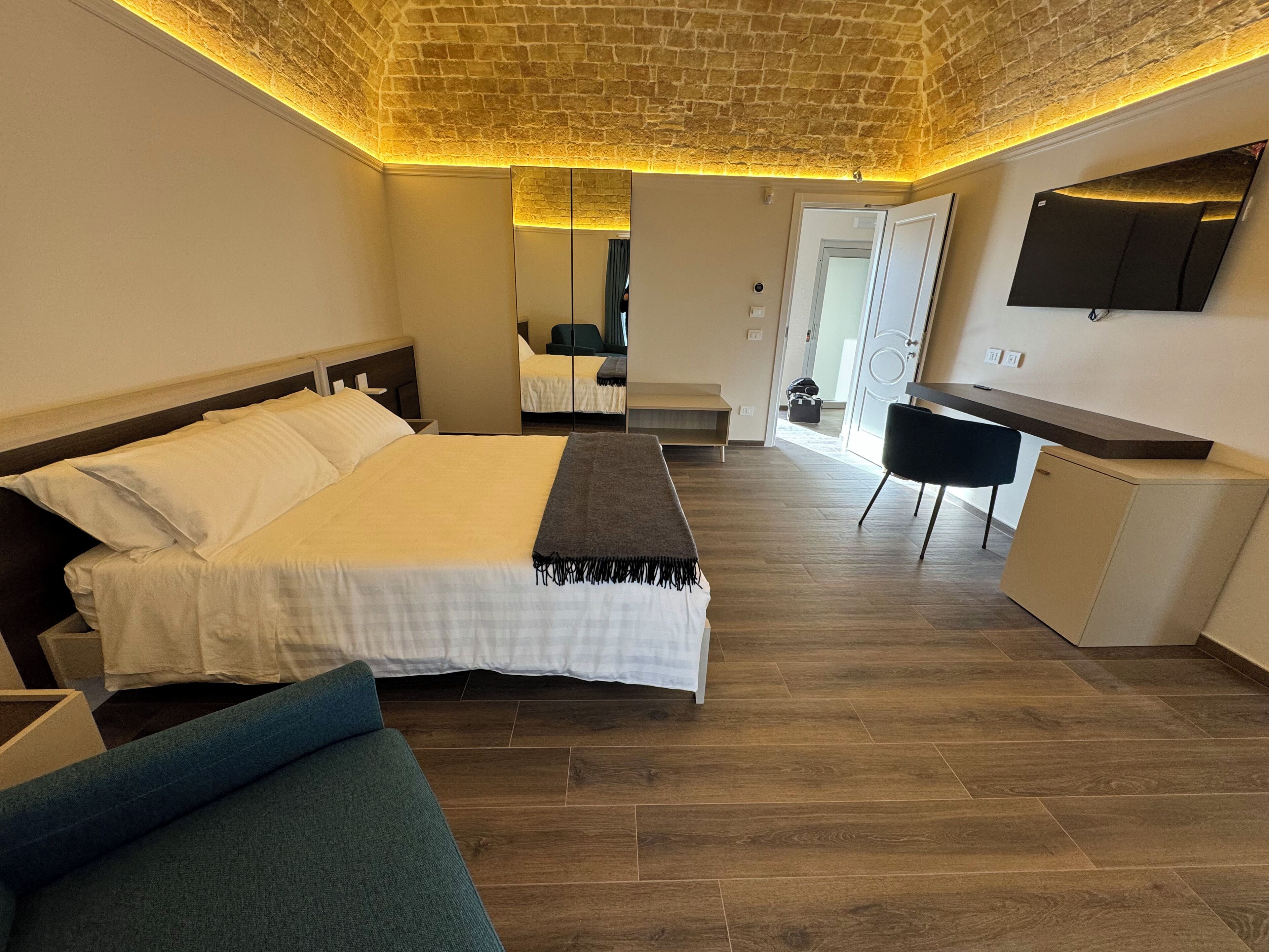 A modern hotel room with a large bed, a desk, a mirror, and a TV.