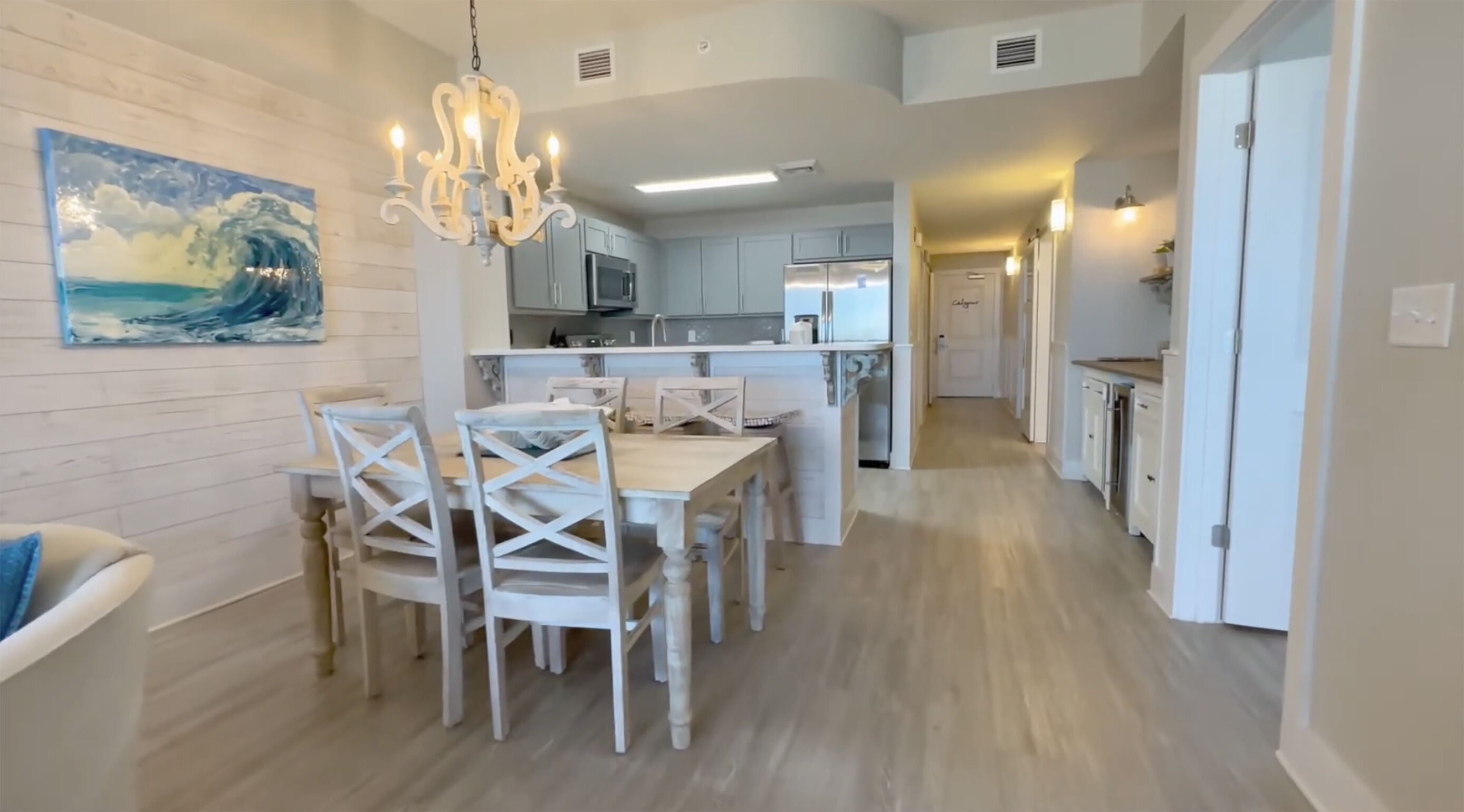 Una cocina moderna con armarios blancos, una isla central y un comedor con mesa y sillas blancas.