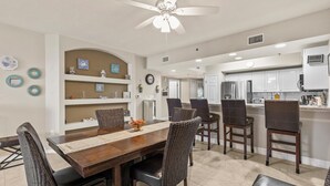A modern kitchen with white cabinets, a central island, and a dining area with dark wooden furniture.