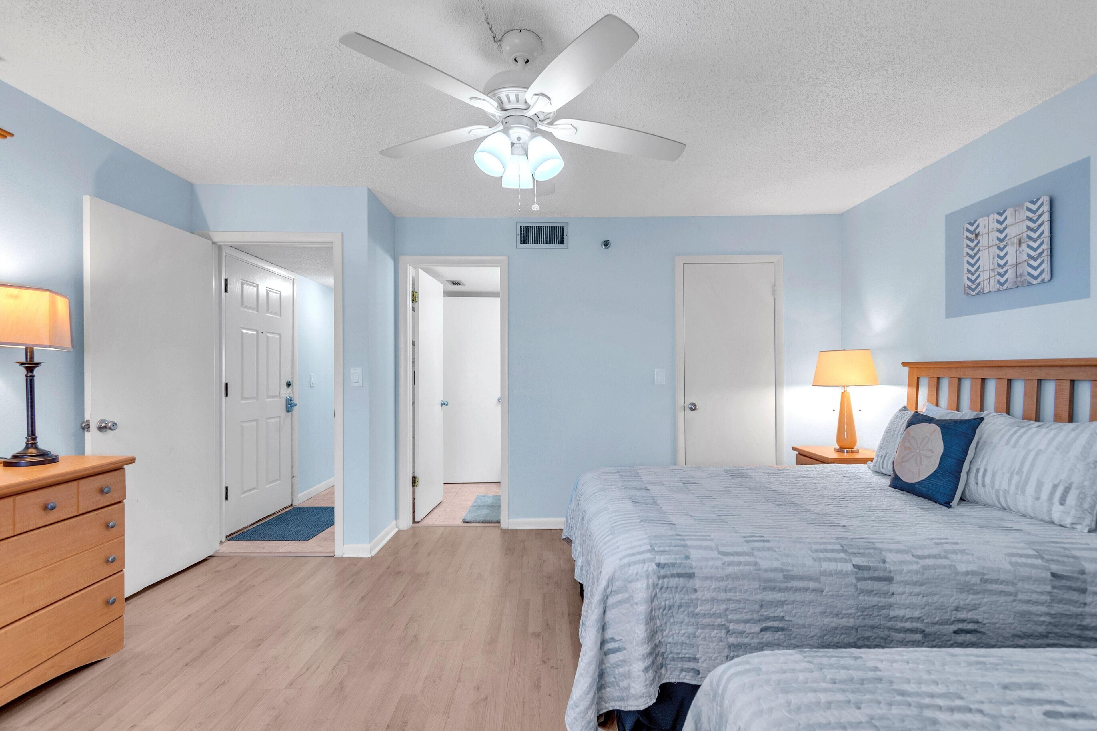 A bedroom with a bed, a nightstand, a dresser, a ceiling fan, and a door leading to another room.