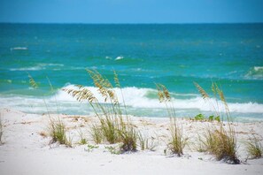 A beach with sand and grass in the foreground and a view of the ocean in the background. - Sea Club #304 - Gone Coastal (Indian Shores)