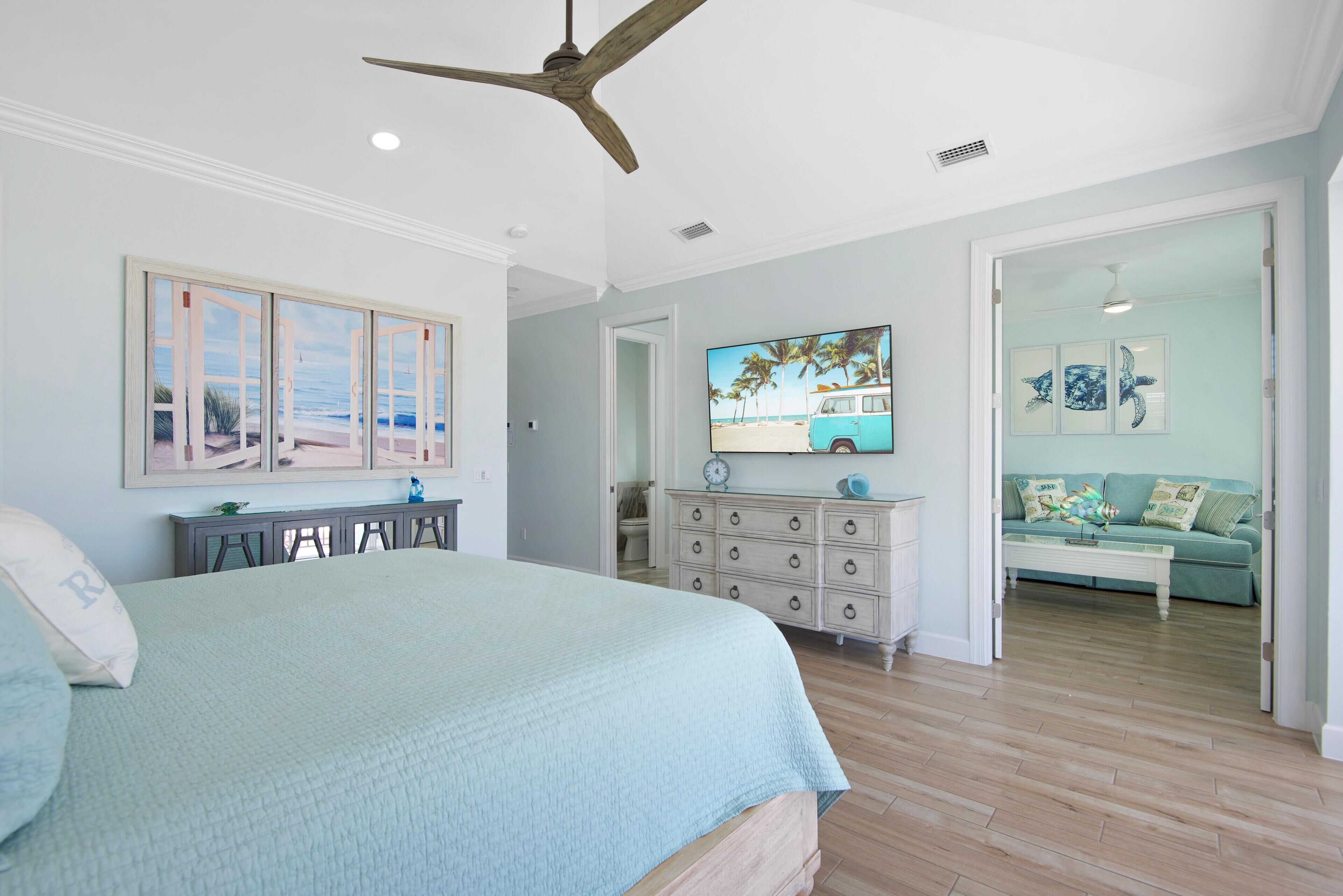 A bedroom with a bed, a dresser, a vanity, and a view of a living room.