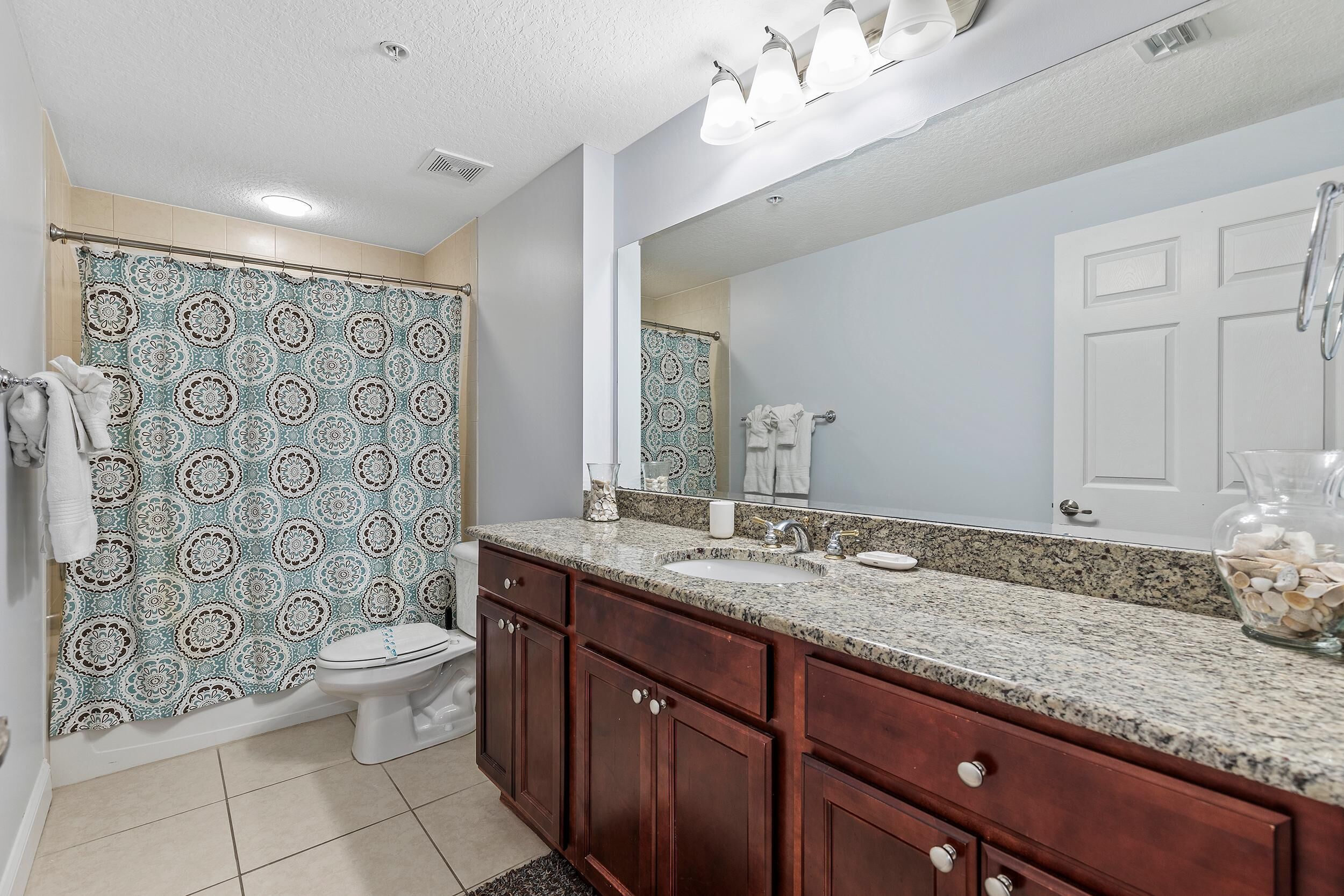 A bathroom with a patterned shower curtain, a sink, a mirror, and wooden cabinets.