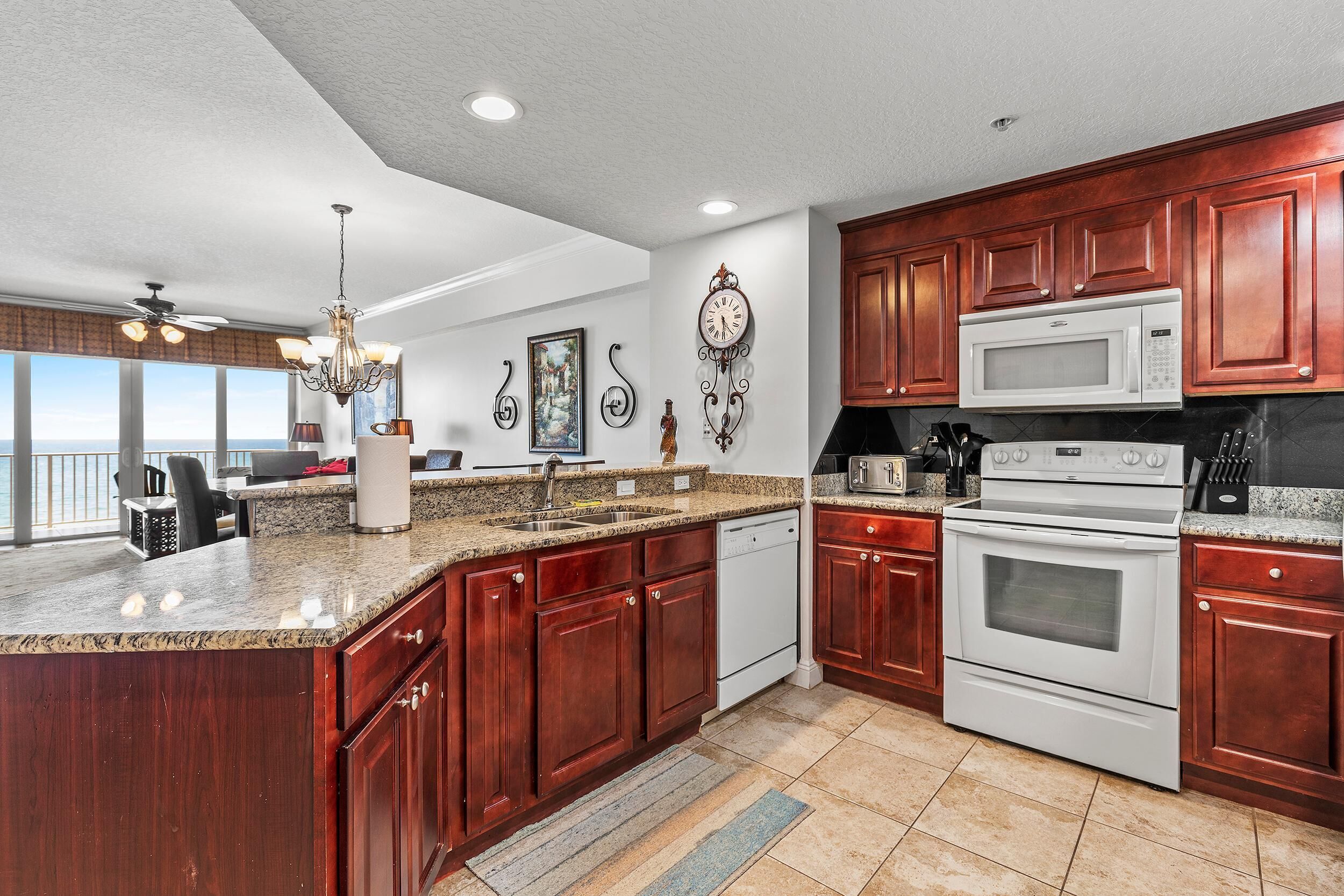 A spacious kitchen with granite countertops, wooden cabinets, a white stove, and a large window overlooking a scenic view.