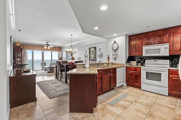 A spacious kitchen with a large island, dark wooden cabinets, white appliances, and a view to the outside.