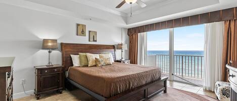 A spacious bedroom with a large bed, a ceiling fan, and a balcony with a view of the ocean.