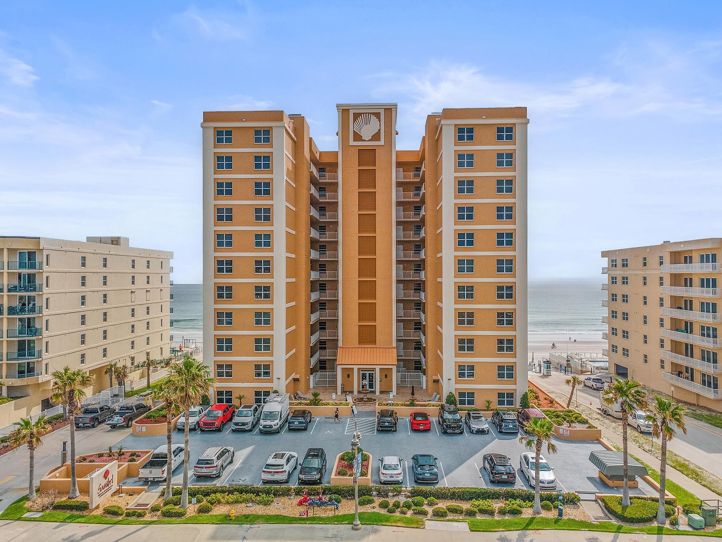 Un hotel de varios pisos con una torre central, estacionamiento y vistas a la playa.