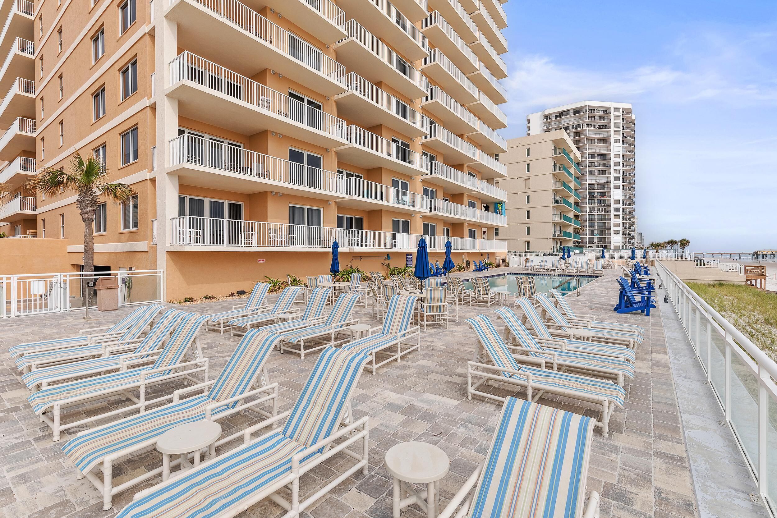 Un hotel con varios balcones, una zona de piscina con tumbonas y vistas al mar.