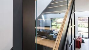 A modern staircase with glass railings and a wooden handrail, leading to a room with a desk and a chair. - Aylesford-house-sleeps 2 & 1 Infant-parking-garden (Aylesford)