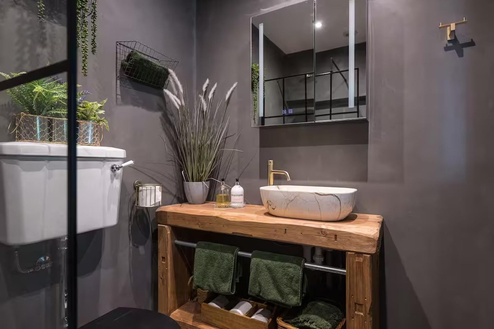 A modern bathroom with a white marble sink, wooden vanity, and a mirror above the sink. There are green towels hanging on a rack below the vanity.