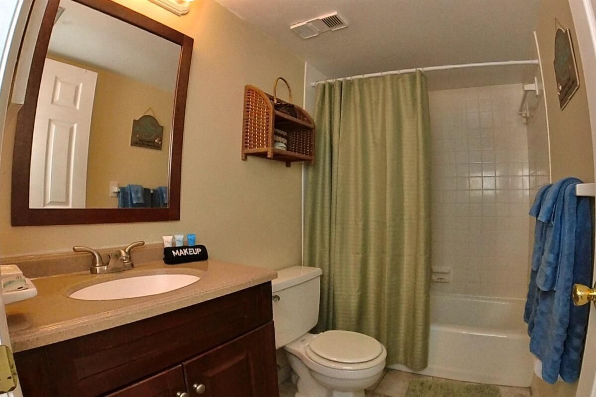 A bathroom with a sink, mirror, and toilet. There is a shower curtain and a towel rack with a towel.