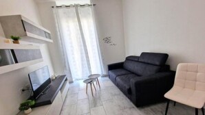 A modern living room with a black sofa, a white chair, a TV on a stand, and a small table with a plant.