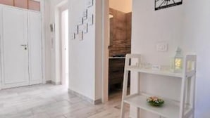 A hallway with a white door, a white shelf with a small plant, and a wall with a geometric art piece.