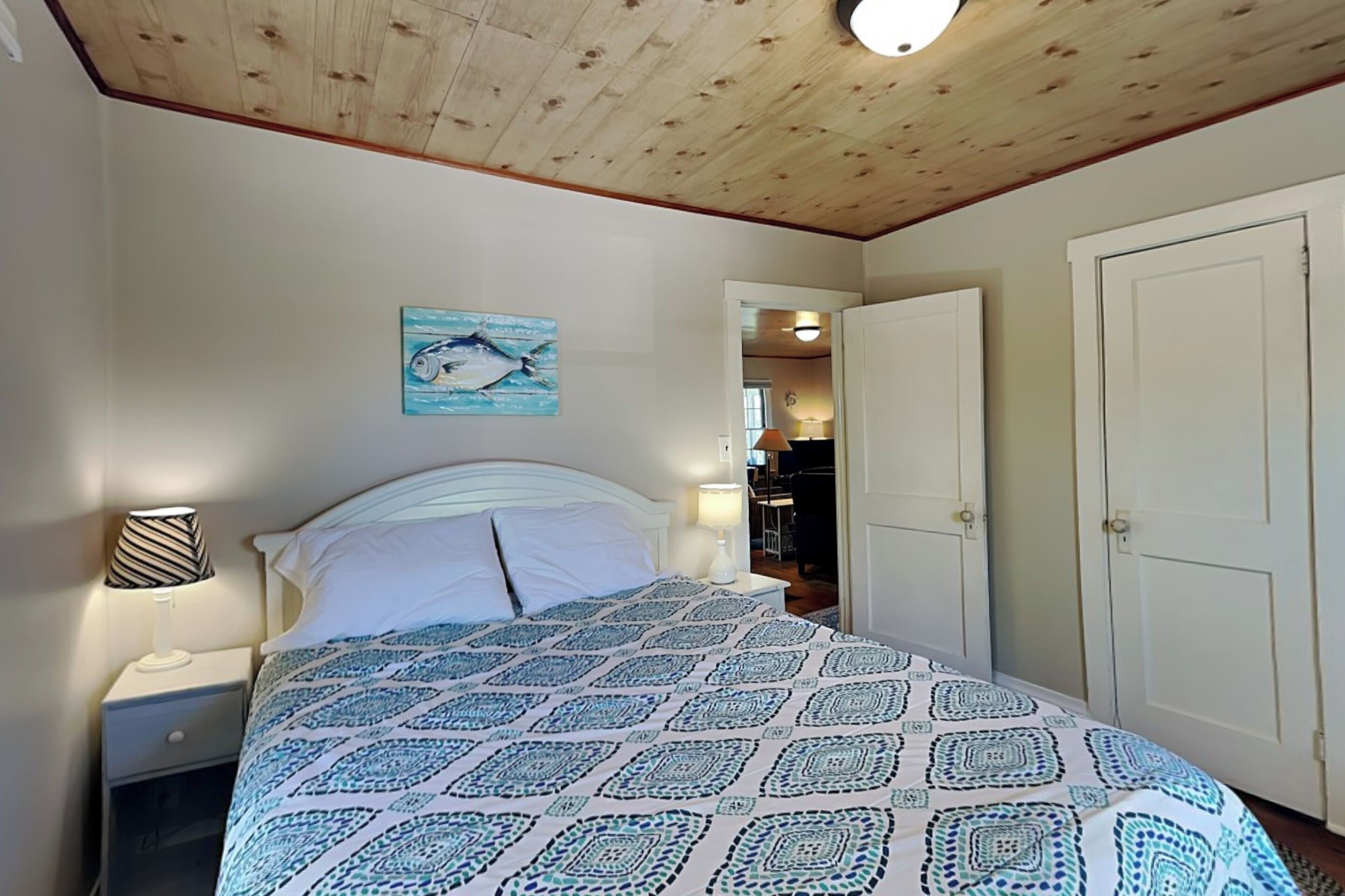 A bedroom with a bed, a nightstand, a lamp, a painting on the wall, and a door.