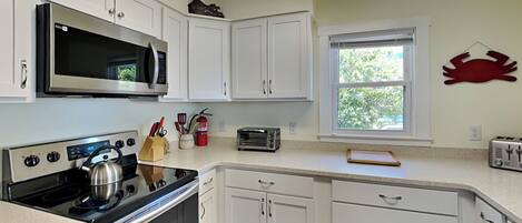 A kitchen with white cabinets, a microwave, a stove, a toaster, and a window with a view of greenery.