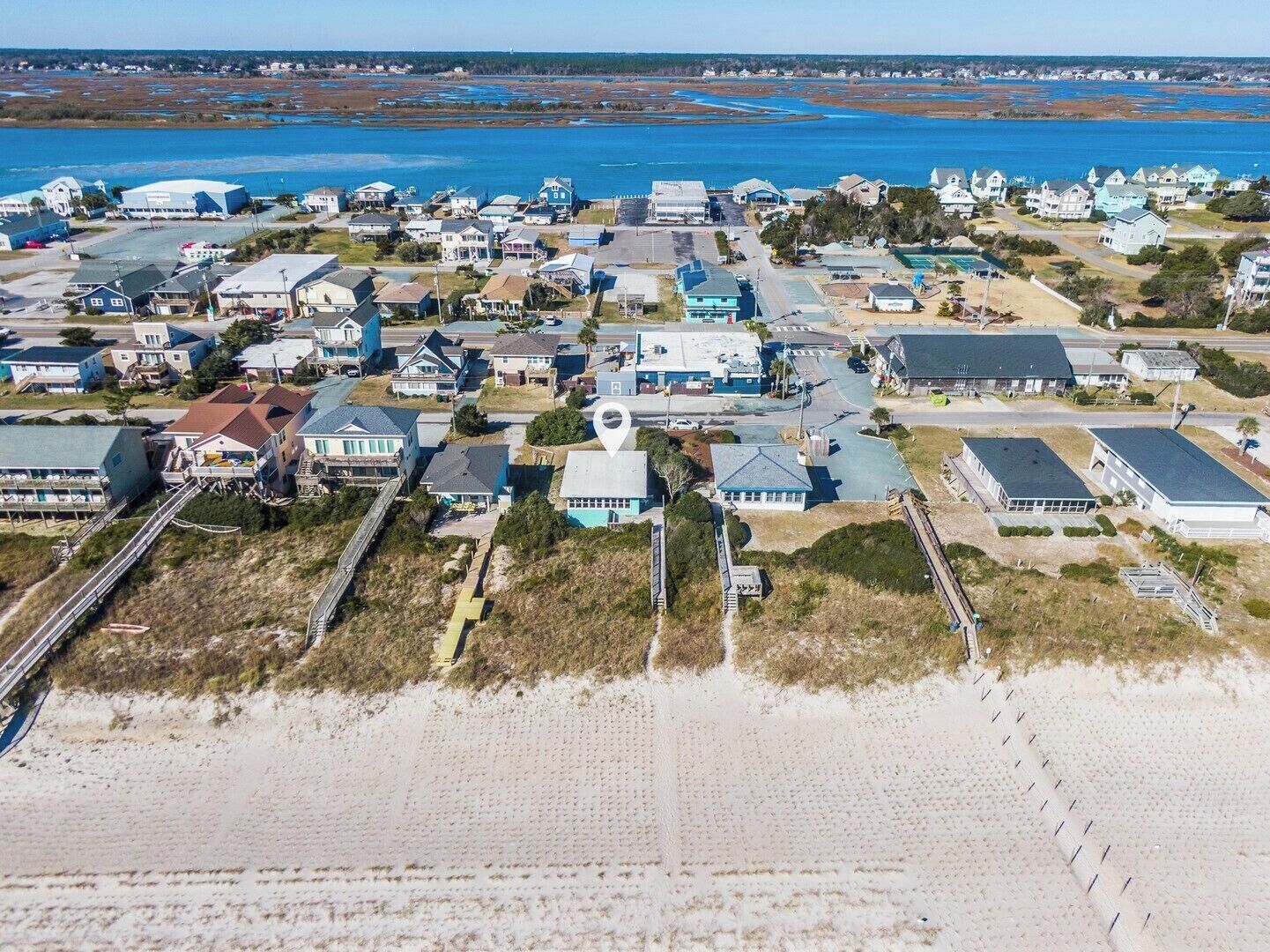 Vista aérea de una zona residencial costera con casas, una playa y una masa de agua al fondo.