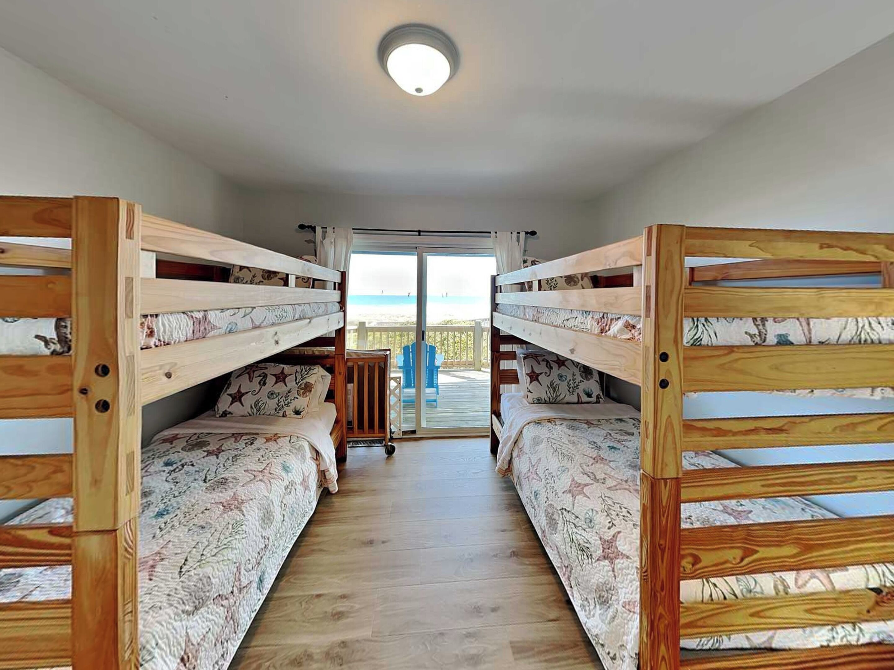 Quarto com beliches, piso de madeira e vista através de uma porta de vidro.