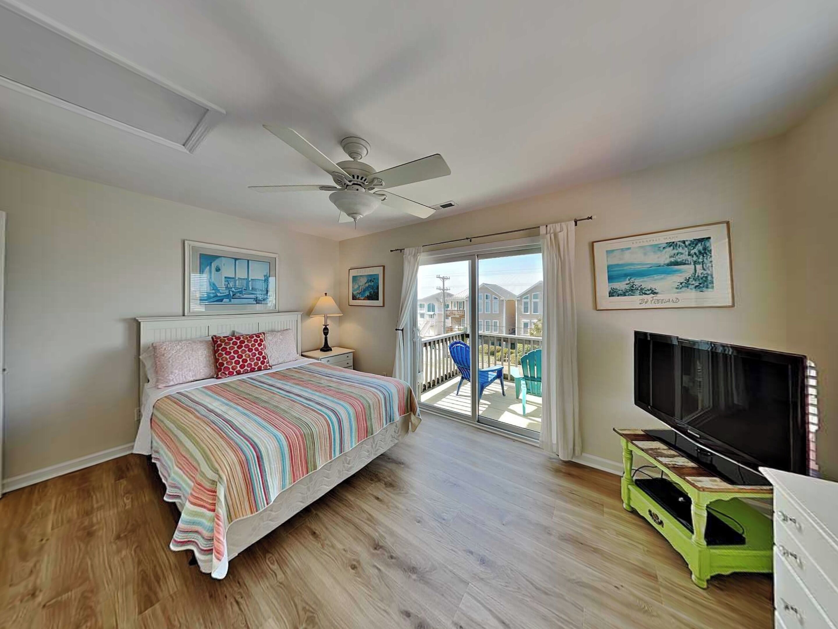 Une chambre à coucher avec un lit, un ventilateur de plafond, une télévision et un balcon équipé de chaises.