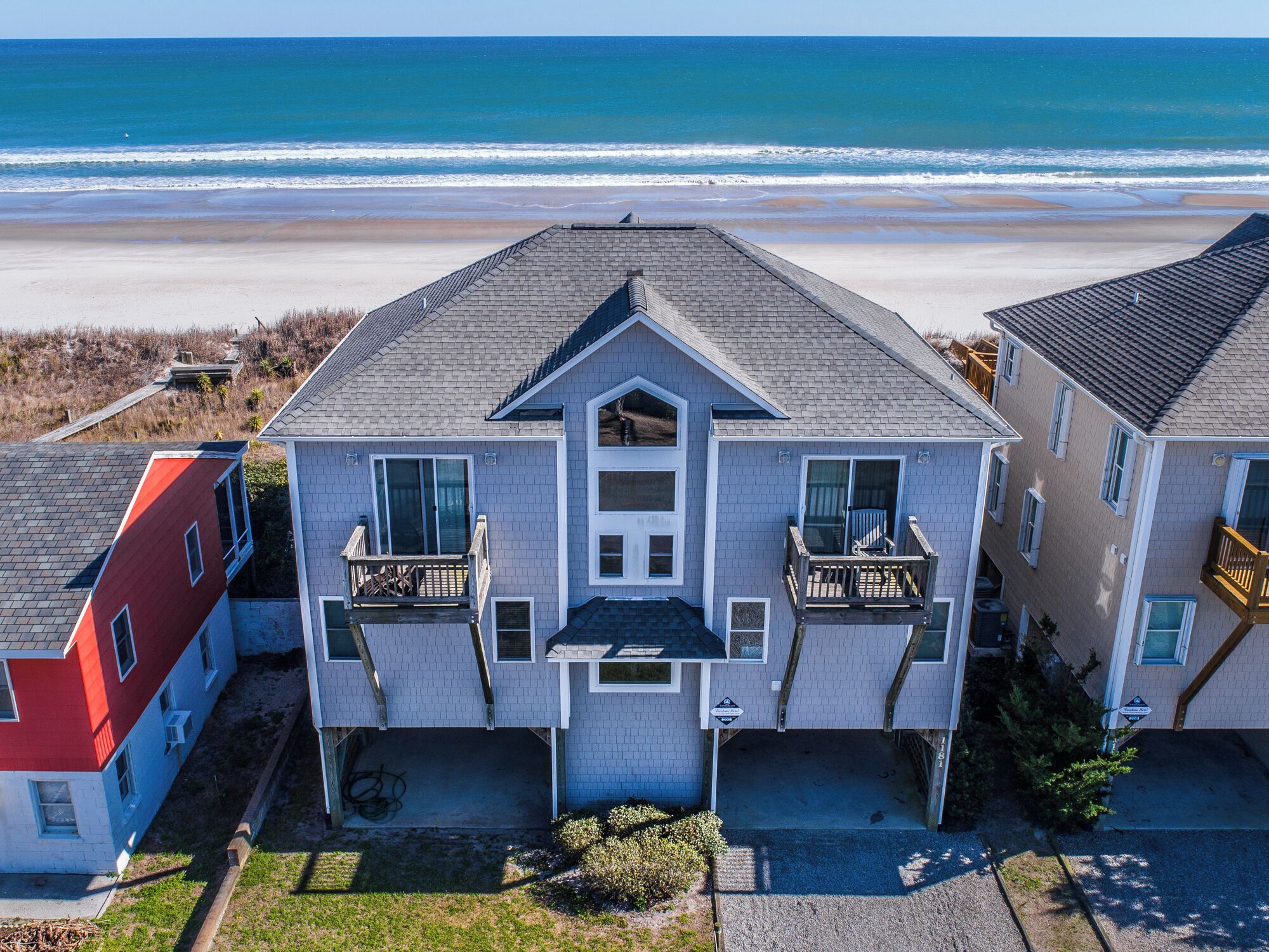 A two-story house with a balcony on the second floor, located near a beach.