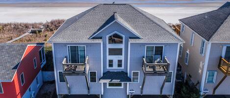 A two-story house with a balcony on the second floor, located near a beach.