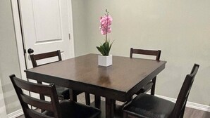 Une table à manger avec quatre chaises, une orchidée en pot et une porte blanche dans une pièce dont le sol est recouvert de parquet.