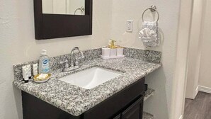 Une salle de bain avec un lavabo surmonté d’un plan de travail en granit, des meubles sombres, un miroir et un porte-serviettes.