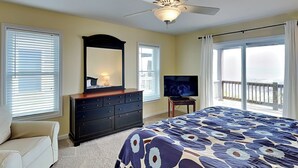 A bedroom with a bed, dresser, TV, and a balcony with a view. - Barefoot Bungalow by Topsail Realty (Holly Ridge)