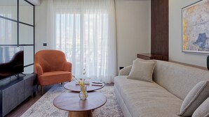 A modern living room with a sofa, armchair, coffee table, and a large window with sheer curtains.