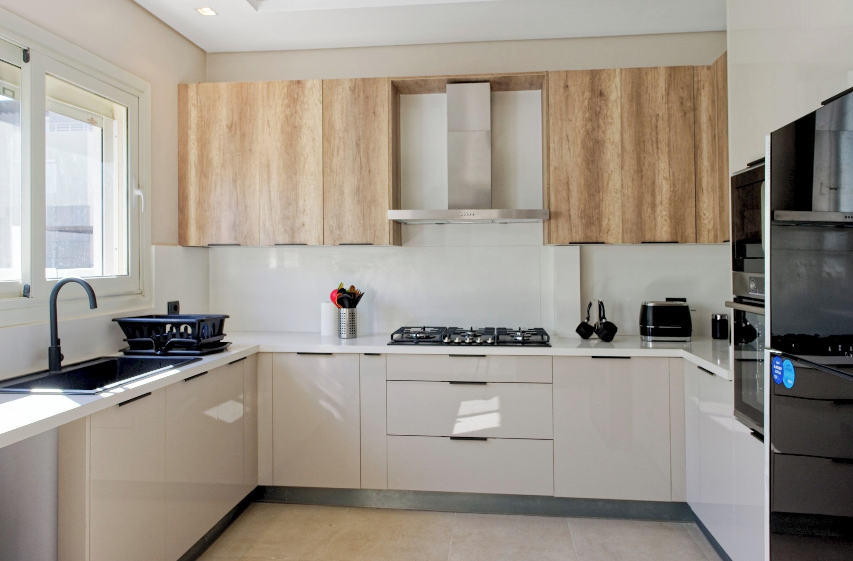 A modern kitchen with white cabinets, a stainless steel range hood, and a built-in oven.