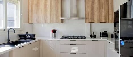 A modern kitchen with white cabinets, a stainless steel range hood, and a built-in oven.