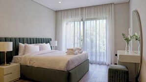 A modern bedroom with a large bed, bedside tables, a vanity with a mirror, and sheer curtains.