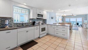 A spacious kitchen with white cabinetry, a microwave, and a view to the living area. - Ponce de Leon Towers 301 (New Smyrna Beach)