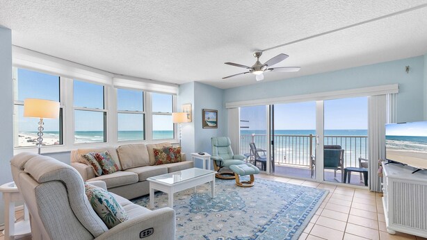 A spacious living room with a large window overlooking the beach, a ceiling fan, and a view to the outside balcony. - Ponce de Leon Towers 301 (New Smyrna Beach)