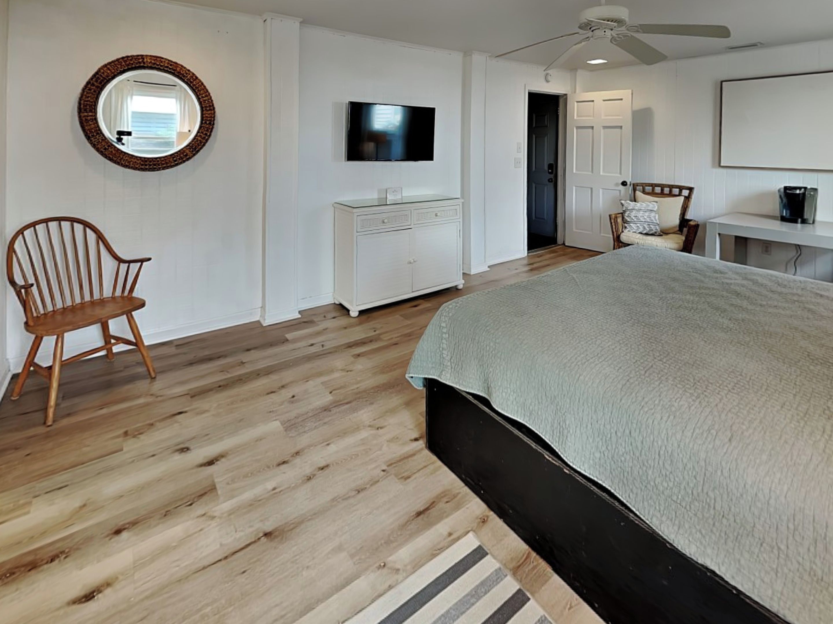 A bedroom with a bed, a chair, a dresser, a television, and a ceiling fan.