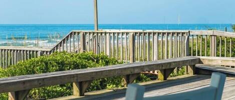 A wooden boardwalk leading to a beach with a bench and a lamp post.