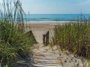 Un sentier en bois mène à une plage, de part et d’autre duquel s’étend une végétation luxuriante.