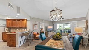 A spacious kitchen with wooden cabinets, a dining area with a large table and blue chairs, and a hanging light fixture.