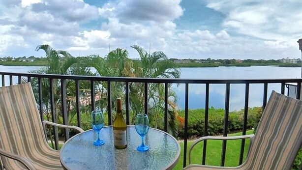 A balcony with a round glass table, two chairs, and a bottle of wine. - Sea Club #104 - Casa con Vista (Indian Shores)