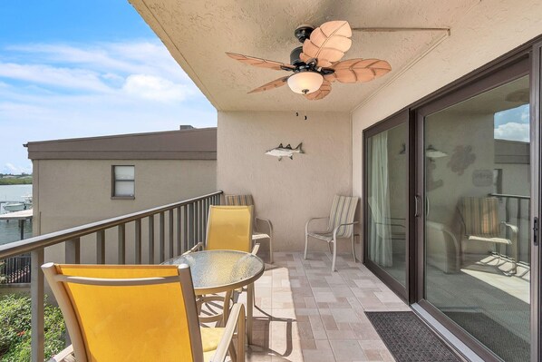 A balcony with a glass door, a ceiling fan, and yellow chairs. - Sea Club #104 - Casa con Vista (Indian Shores)