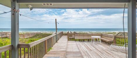 A wooden deck with a view of the beach, a bench, and a table.
