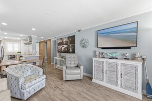 A modern living room with a sofa, armchair, and a large flat-screen TV. - Sea Coast Gardens II 109 (New Smyrna Beach)