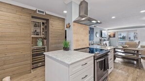 Una cocina moderna con un enfriador de vino empotrado, una campana extractora de acero inoxidable y un comedor con banco y mesa.