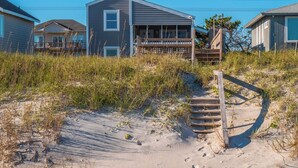 A beach house with a covered porch and a wooden staircase leading to a deck. - Blue Crab by Topsail Realty (Holly Ridge)