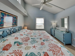 A bedroom with a bed, a dresser, a ceiling fan, a window, and a wall with a framed picture. - Blue Crab by Topsail Realty (Holly Ridge)
