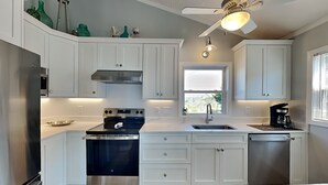 A modern kitchen with white cabinets, a stainless steel oven, a coffee maker, and a window with a view. - Blue Crab by Topsail Realty (Holly Ridge)