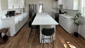 A modern kitchen with white cabinetry, a central island with stools, stainless steel appliances, and a wooden floor. - Hereford Motel (Albany)