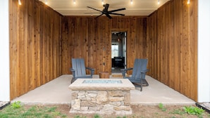 A covered patio area with two chairs and a table, wooden walls, a ceiling fan, and a stone accent wall. - Hereford Motel (Albany)
