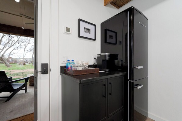 A compact kitchen with a black refrigerator, a coffee maker, and a small countertop with bottles and a tray.