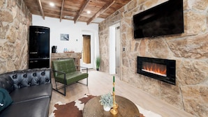 A cozy living room with a stone wall, a fireplace, a flat-screen TV, a leather sofa, and a green chair. - Hereford Motel (Albany)